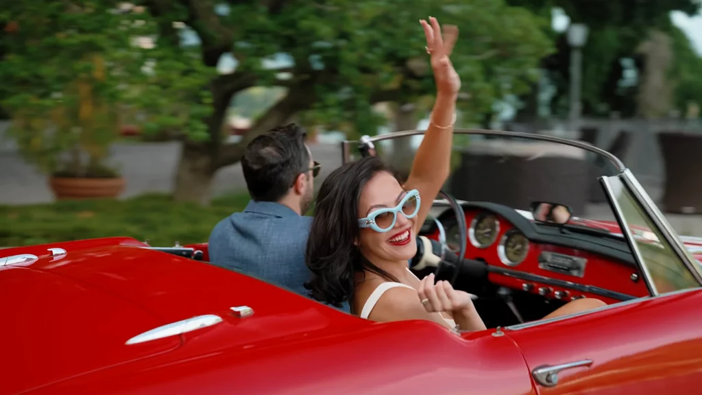 Engaged couple waving from a red vintage convertible on Lake Como in a save the date video